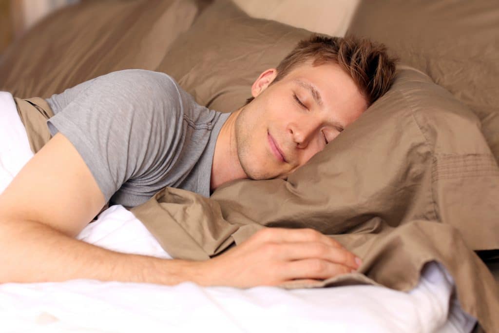 Young man sleeping in bed smiling, Better Sleep Council