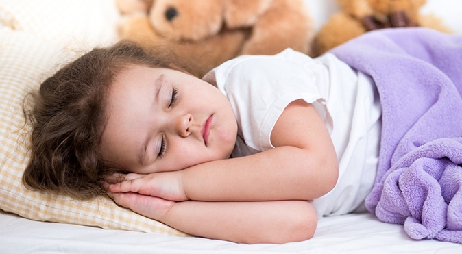 Little girl sleeping in bed with purple blanket, Better Sleep Council