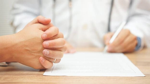 hands folded over legal document while someone else signs the bottom of the document