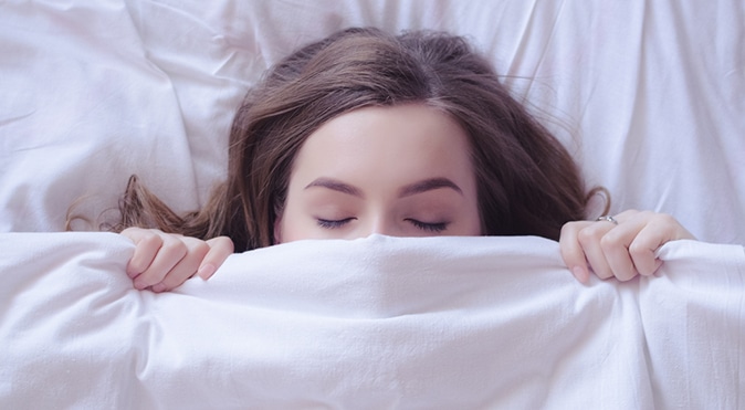 Woman pulling covers up half-way over her face, Better Sleep Council