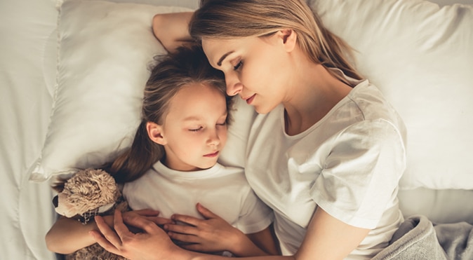 Mother and daughter with teddy bear snuggling in bed, Better Sleep Council