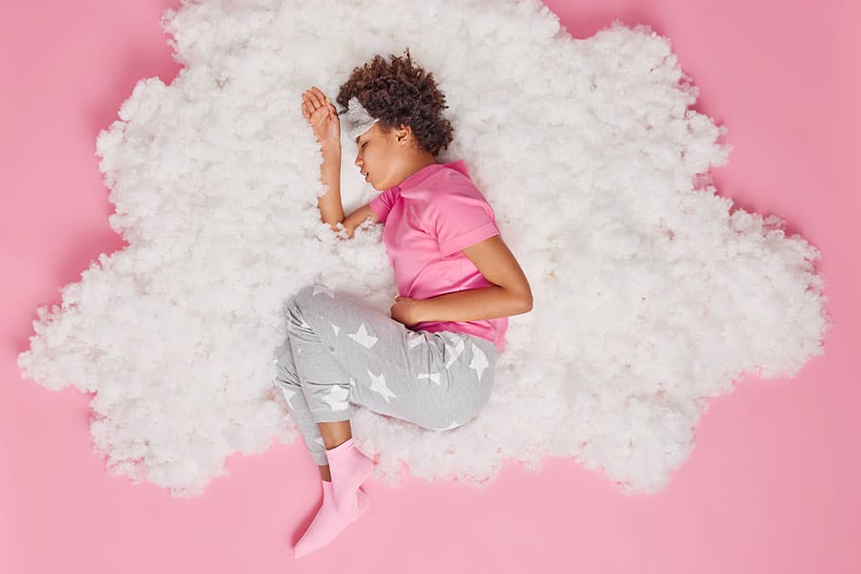 Sick African American woman cannot sleep because of strong pain in belly suffers from stomachache indigestion feels unwell dressed in pajama poses on white cloud. Health problems and sleeping concept