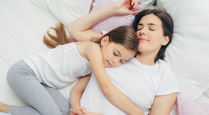 Mother and daughter cuddling in bed, Better Sleep Council